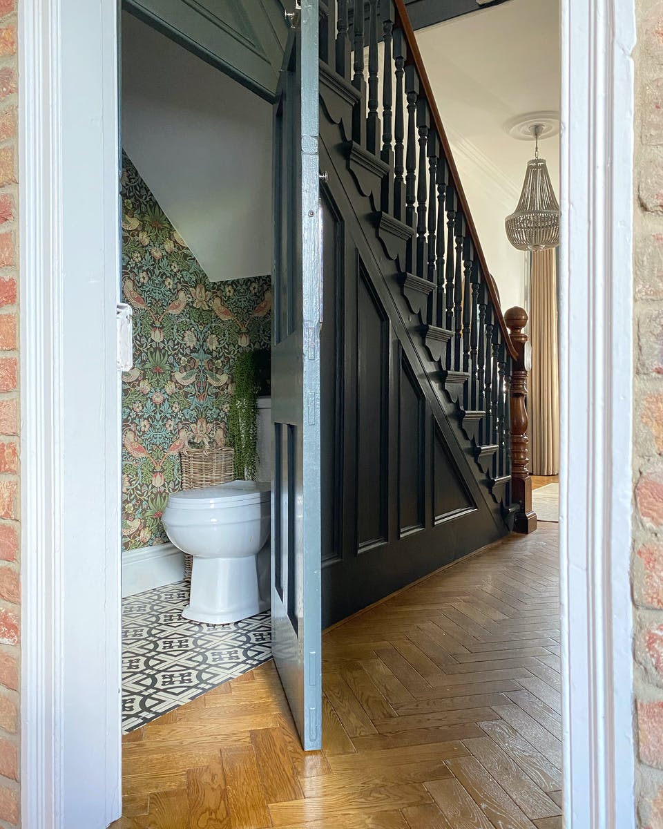 Hidden toilet under the stairs with patterned wallpaper on walls