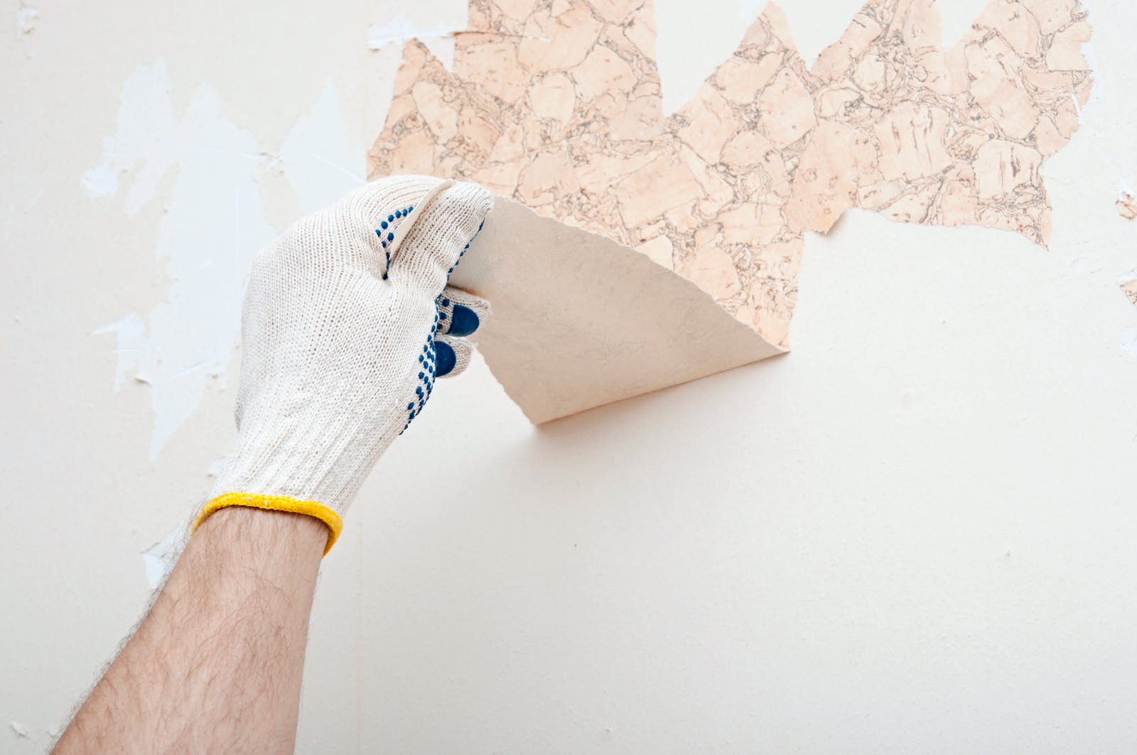 Person peeling off wallpaper from wall after using steamer