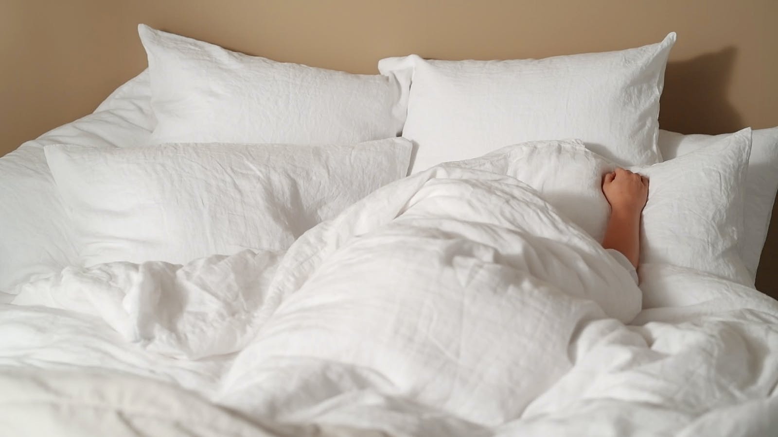 Person hiding under the white linen duvet with Lick paint Beige 02 painted walls