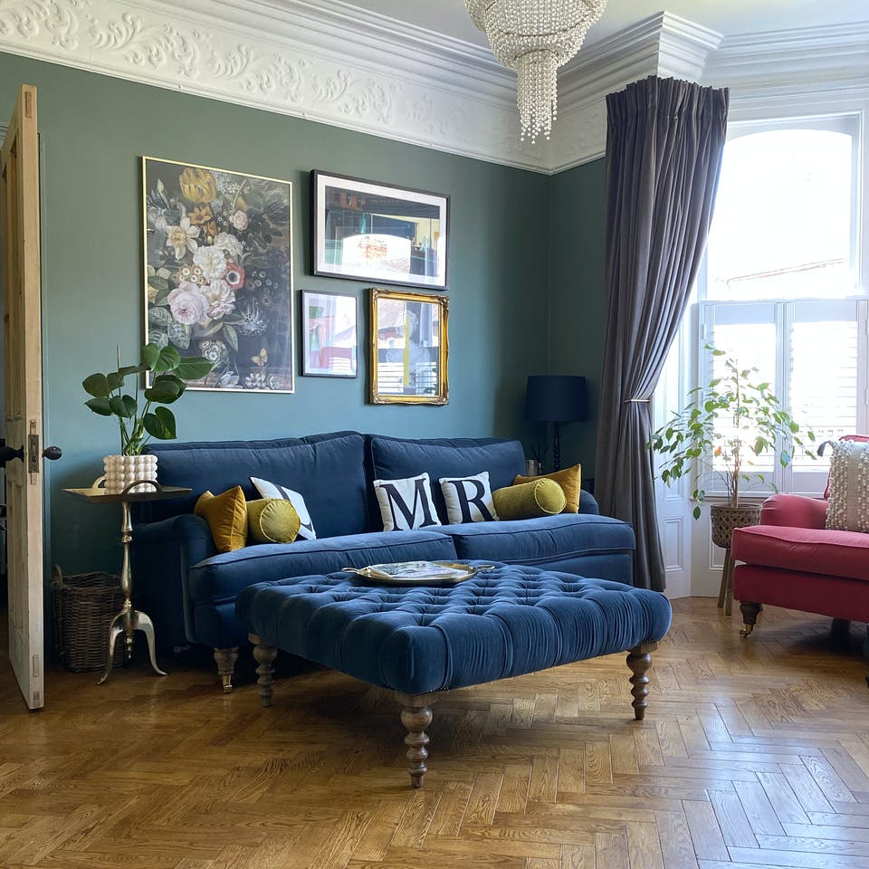 Green living room with blue velvet sofa and bay windows