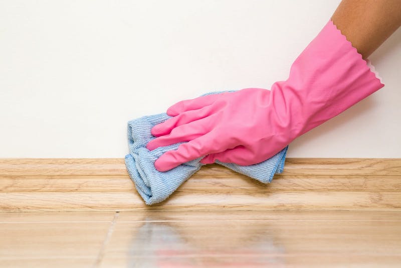 hand wearing washing up gloves wiping skirting board with sponge