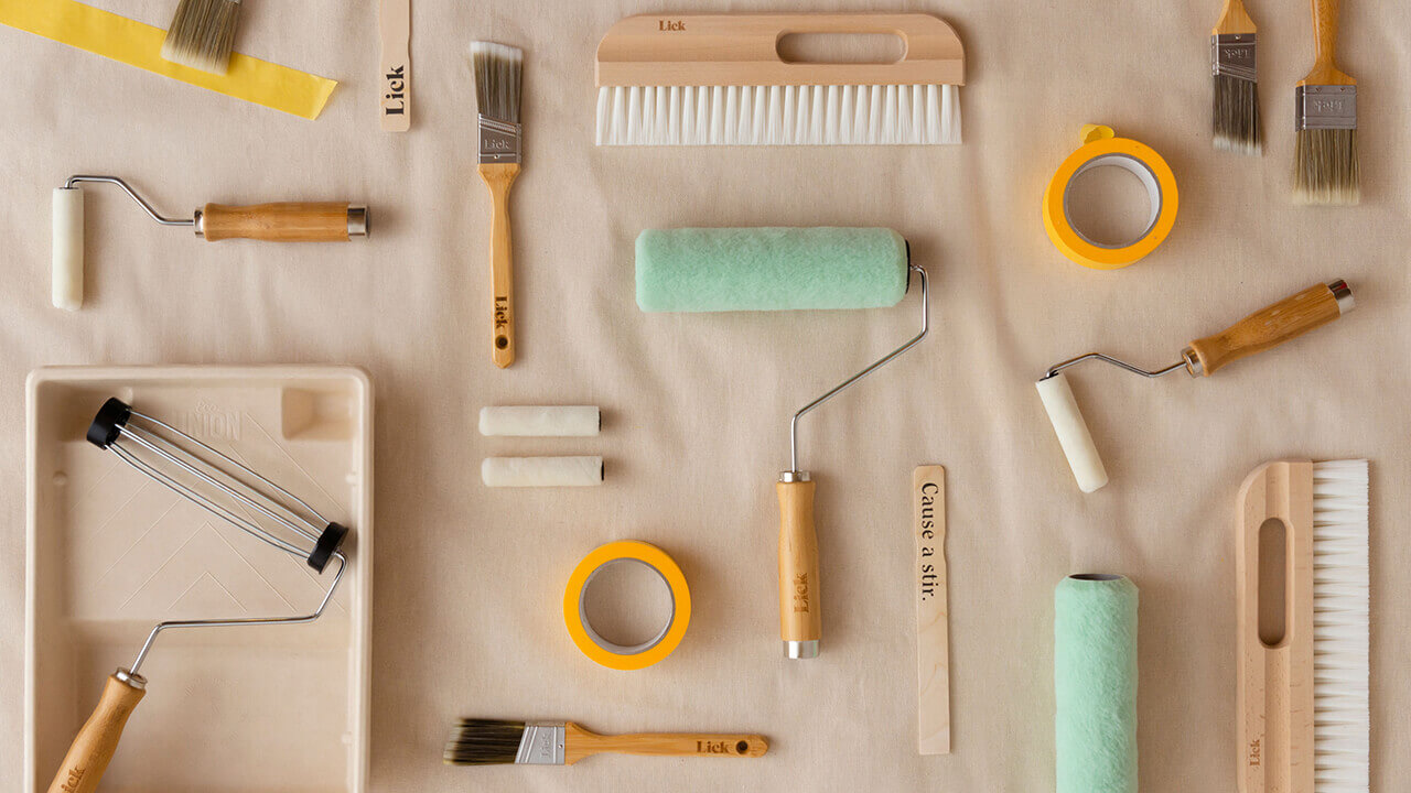 Image of lick home painting supplies on a biodegradable dust sheet such as paint brushes, paint rollers, pulp paint tray, roller sleeves, wallpaper brush, painters masking tape all made from sustainable materials