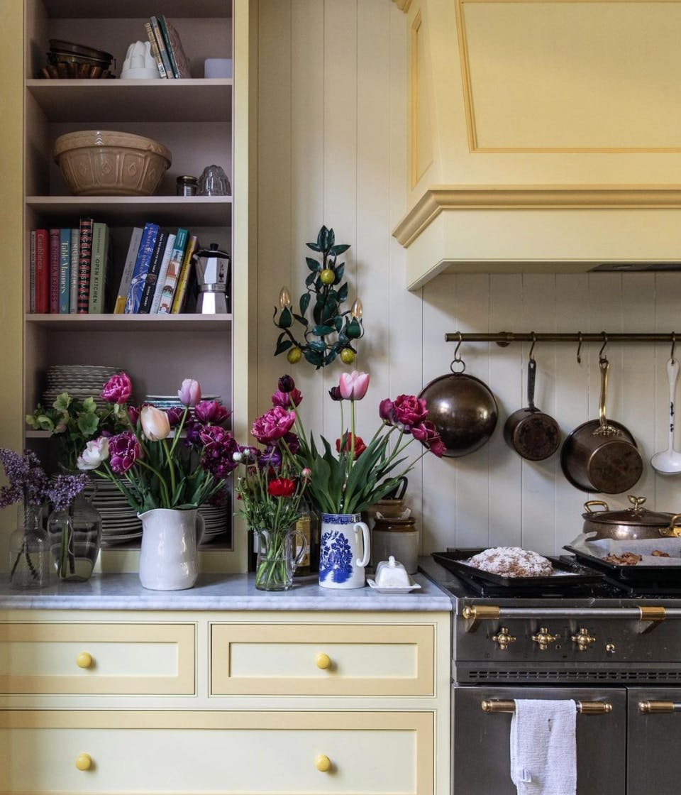 Cottage core kitchen with yellow cabinets and open shelving with flowers in vases
