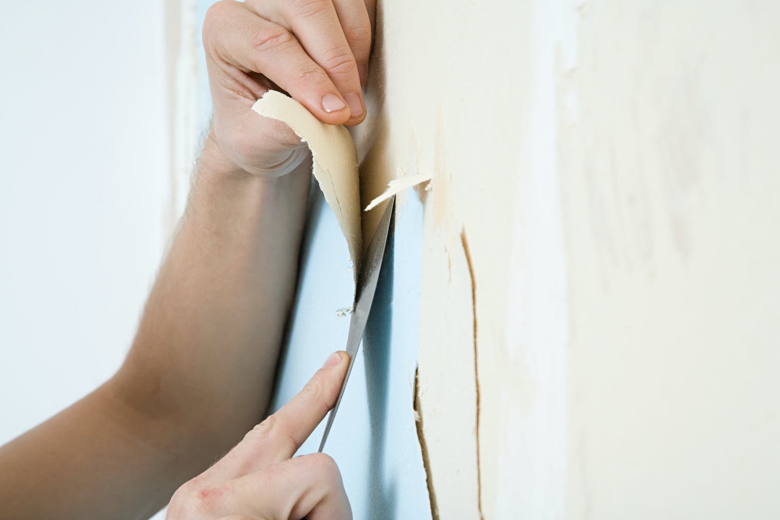 Person using wallpaper scraper to remove wallpaper from a wall